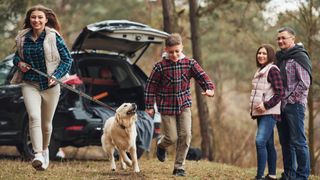 Family giving dog a run near their car during rest break on journey