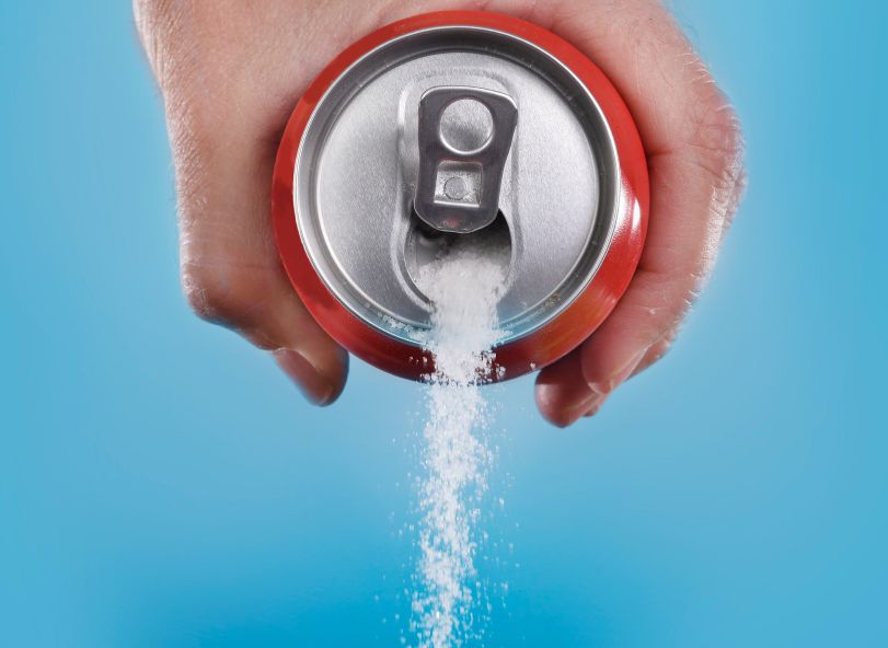 Hand pouring sugar from a soda can.