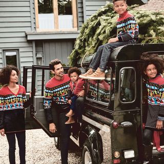 A man, woman, and three young children wear matching Christmas jumpers posed next to a black Land Rover Defender.