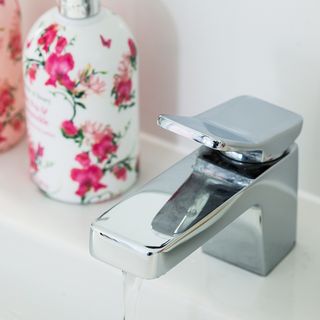 close up of a running bathroom tap with a flowery soap bottle
