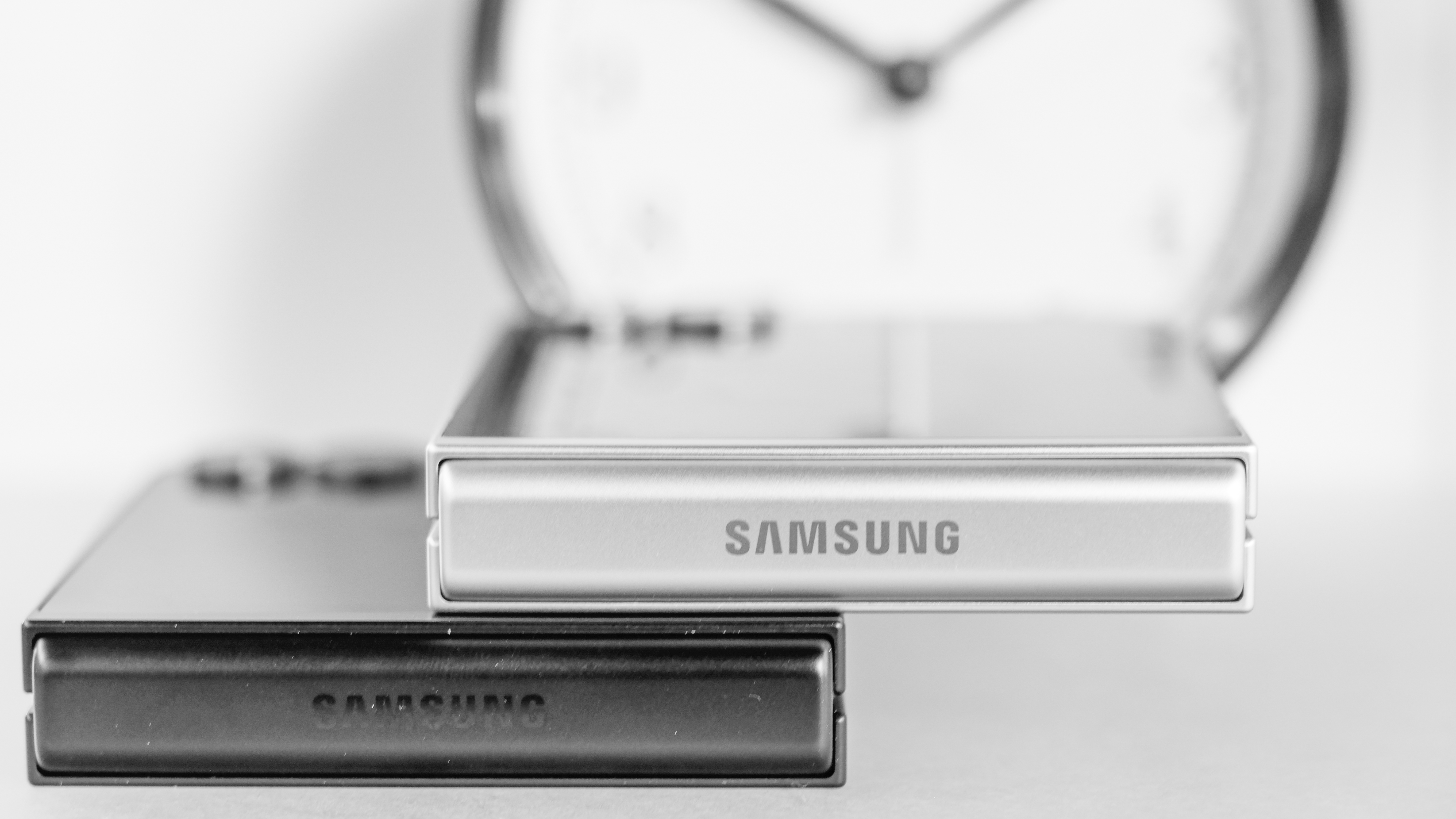 Two closed Samsung Galaxy Z Flip 7 devices in white and black on top of each other showing Samsung logo on hinge