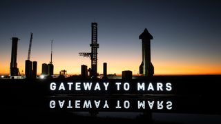 a rocket booster and upper stage are positioned vertically against a dusky sky, behind a white light-up sign that says "gateway to mars."