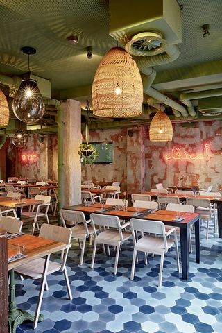 Restaurant with tables, chairs, patterned coloured walls, blue checkered floors and large pendant lights at Bar Skuka, Frankfurt, Germany.
