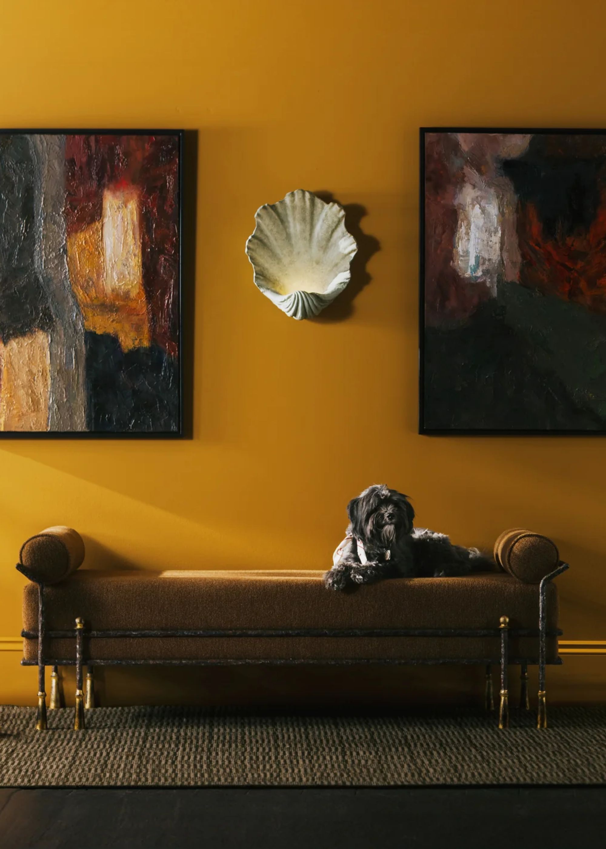 Shell lighting in between two framed pieces of art with a bench below the artwork. On the bench is a dog, laying down on the bench.