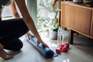 How to do a home workout: Close up of young Asian sports woman practicing yoga / exercising at home. Unrolling yoga mat, getting prepare to work out in the fresh bright morning