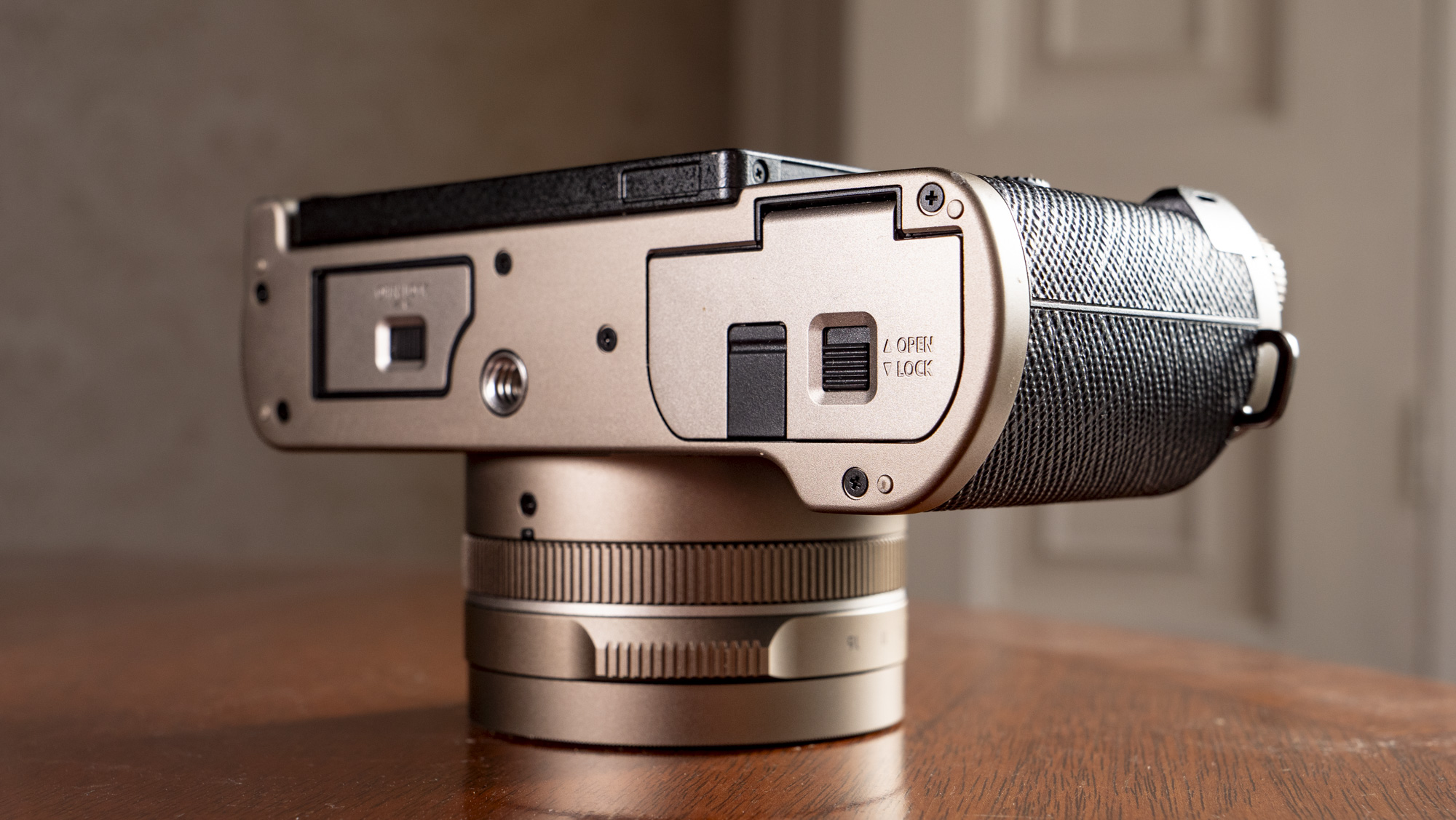 The underside of the Titanium Gold special edition of the Panasonic Lumix L10 compact camera, on an antique wooden table 