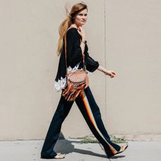 Street style shot of Eugenie Trochu wearing a lace-hem top, tan Chloe bag with rainbow fringe, rainbow stripe track pants, and sandals