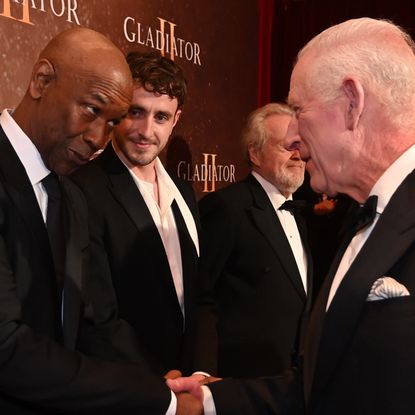 Denzel Washington wears a black suit while shaking hands with King Charles who is wearing a tuxedo