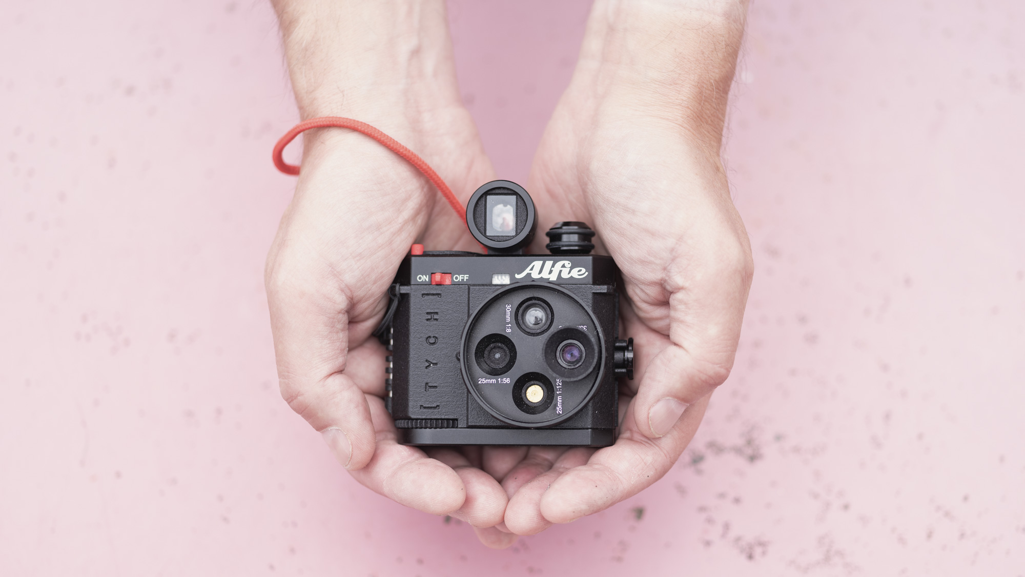 Alfie Tych camera in hands over a pink surface