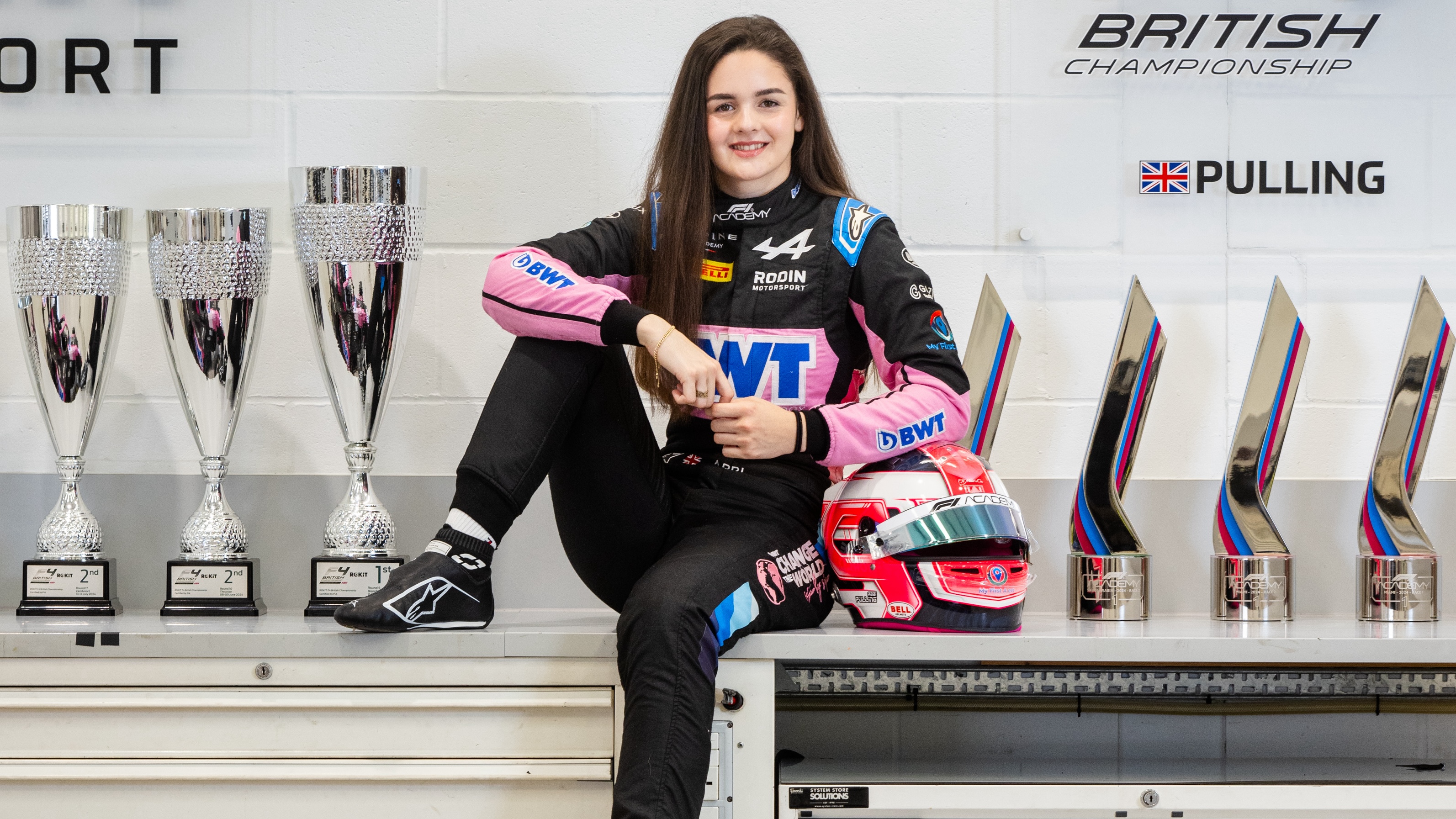 Girl in racing overalls surrounded by trophies