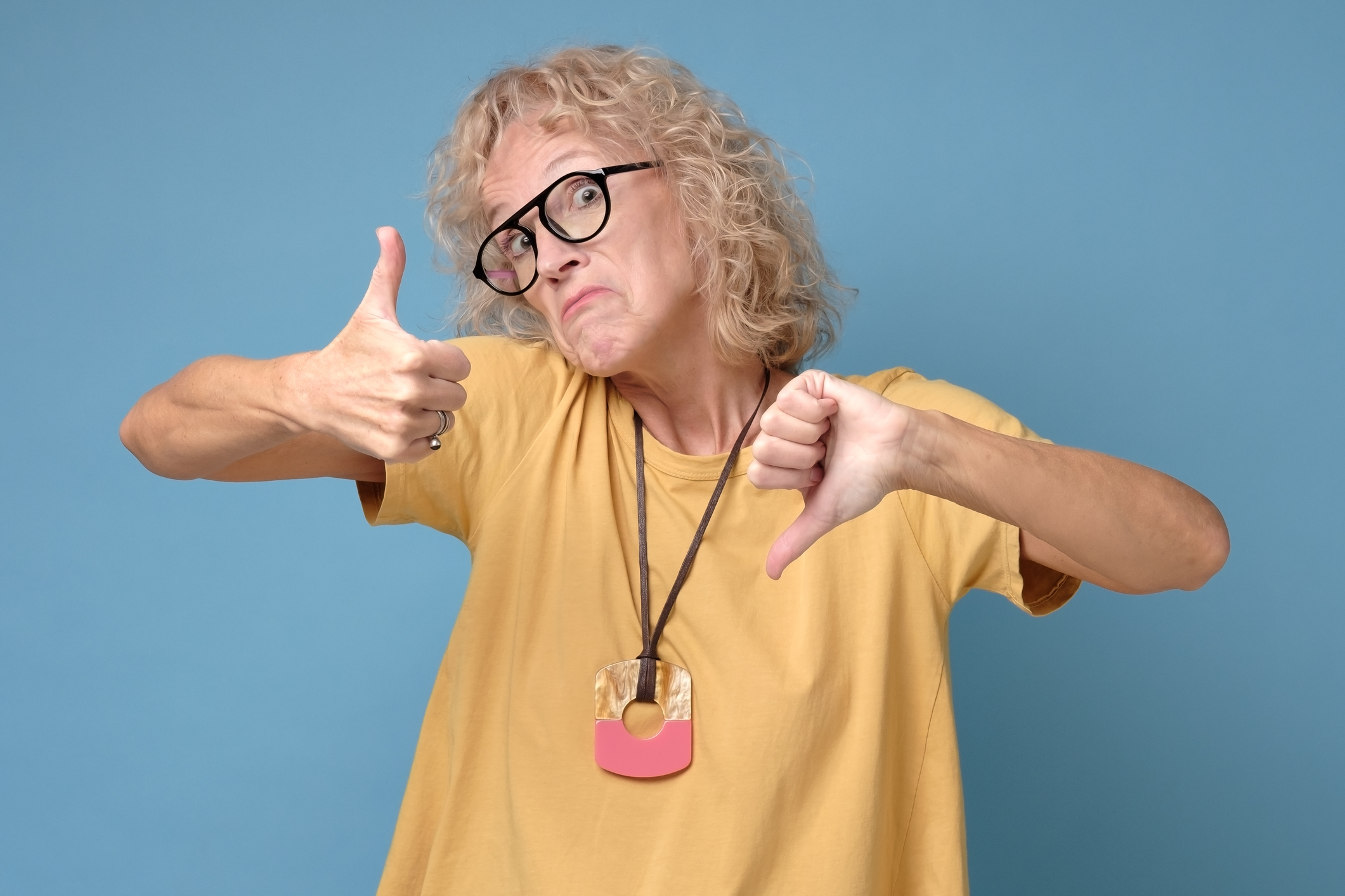 Disappointed skeptical attractive woman unsatisfied, showing thumbs down and up frowning in doubt. I do not know what to choose. Studio shot