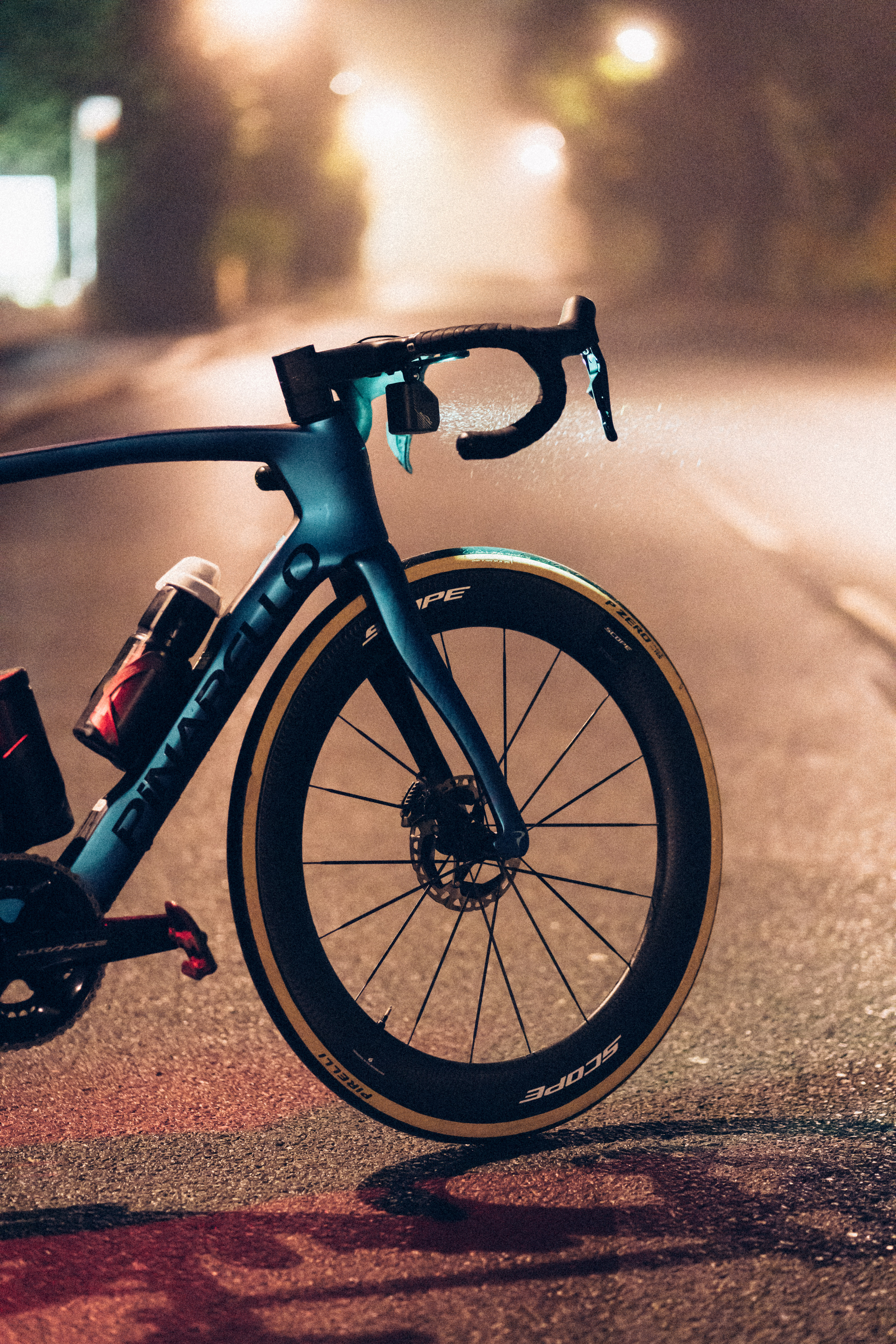 A close up of a blue pinarello at night in fog, with the front light projecting a cone of light forwards.