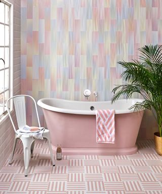 Playful pastel bathroom scheme with rainbow pastel wall tiles, pink and white stripe floor tiles, and coordinating freestanding pink bath