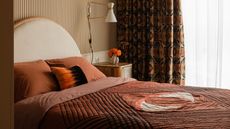 a bedroom with striped wallpaper, a semi circle bedhead, and burl sideboard furniture