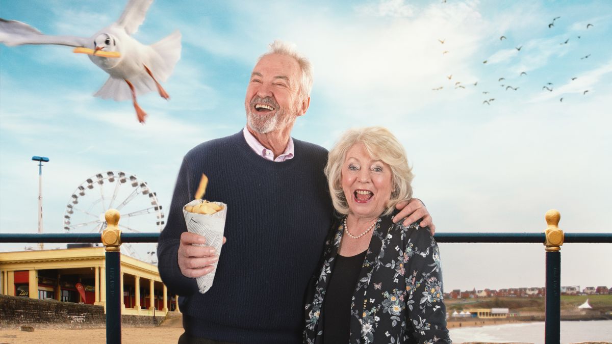 Larry Lamb holds a cone of chips as a seagull flies off and Alison Steadman stands next to him against a seaside backgrounds in Alison &amp; Larry: Billericay to Barry.