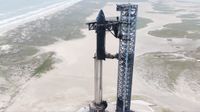 a huge black and silver rocket stands amid dunes next to the ocean