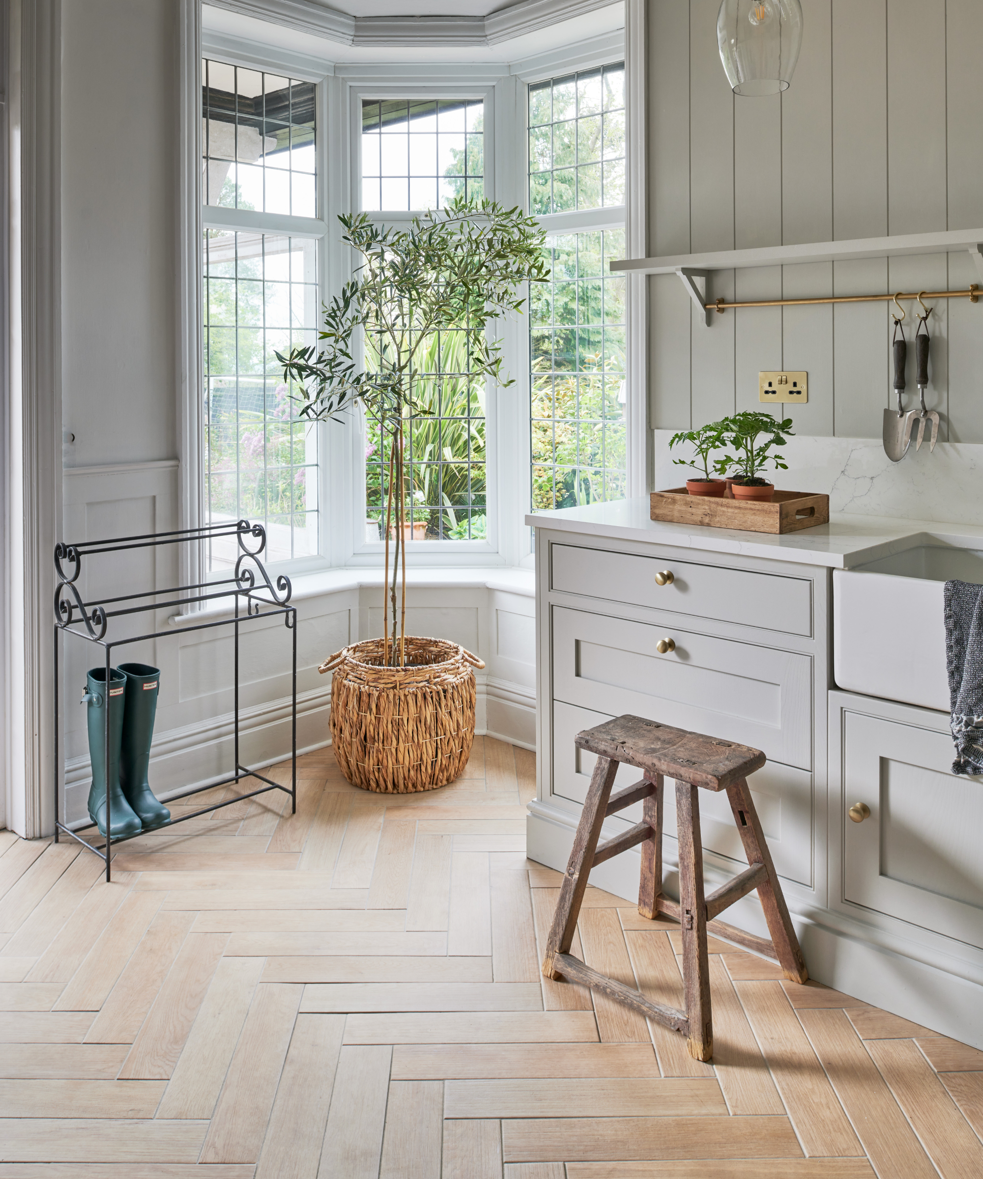 porcelain wood effect tiles laid in herringbone pattern in utility area with large bay window, welly rack and sink in pale grey units