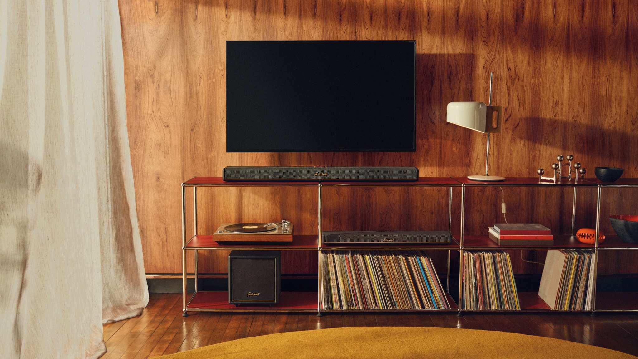 A lifestyle shot of the Marshall Heston 60 and Sub 200 on open shelving below a reasonably small TV