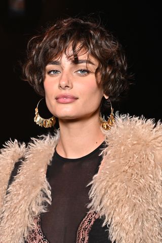 Taylor Hill with a curly bob an a feathered vest.