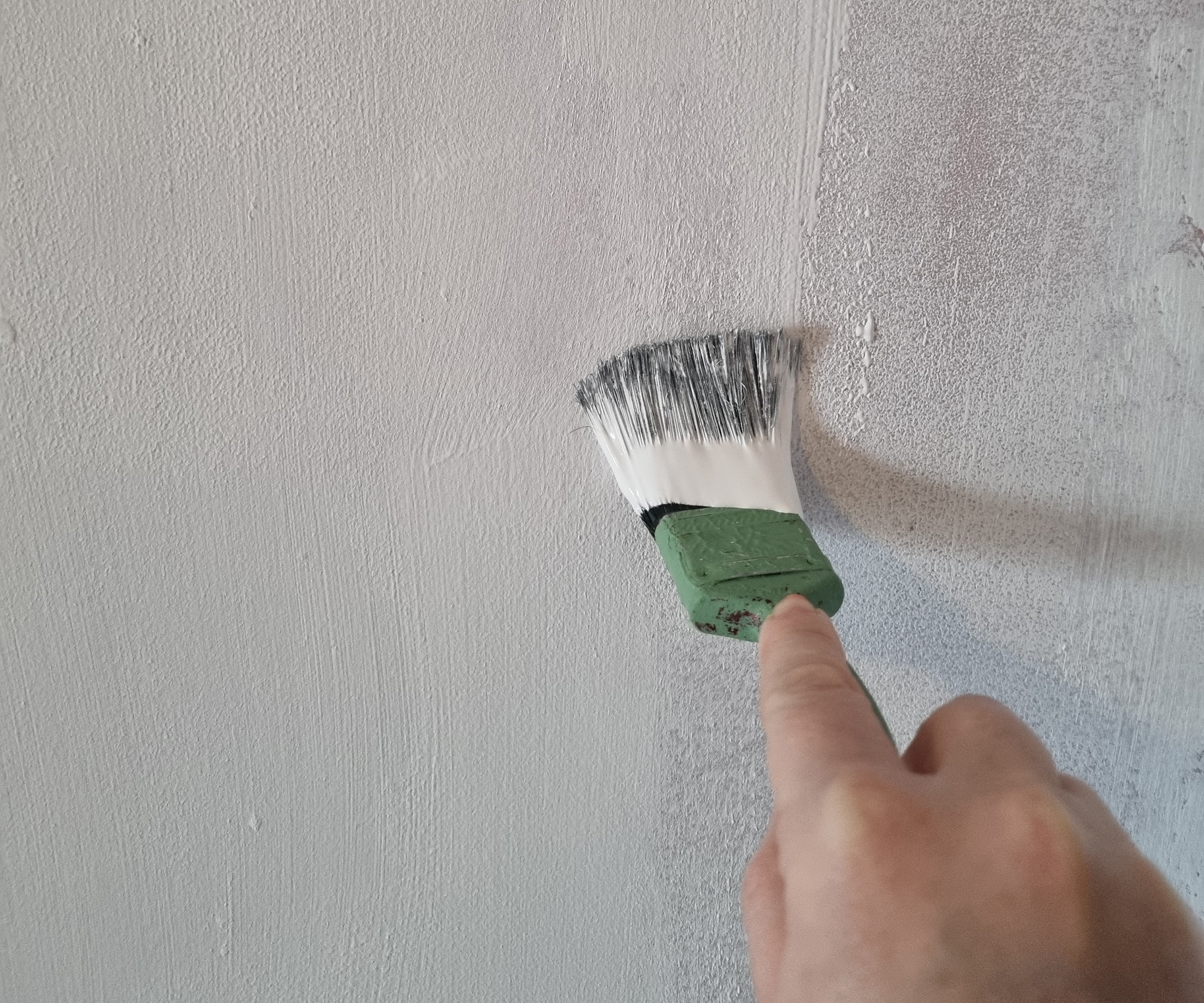 hand painting white anti-condensation paint onto a wall with a paintbrush