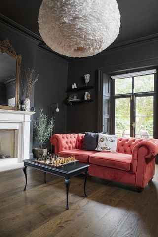 Black living room with wooden floor, red Chesterfield sofa, black coffee table with chess board and oversized feather ceiling light