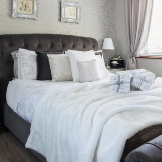 Grey and white neutral bed with many pillows, cushions and fluffy throw blanket