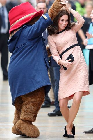 Kate Middleton in a pink dress dancing with Paddington Bear.