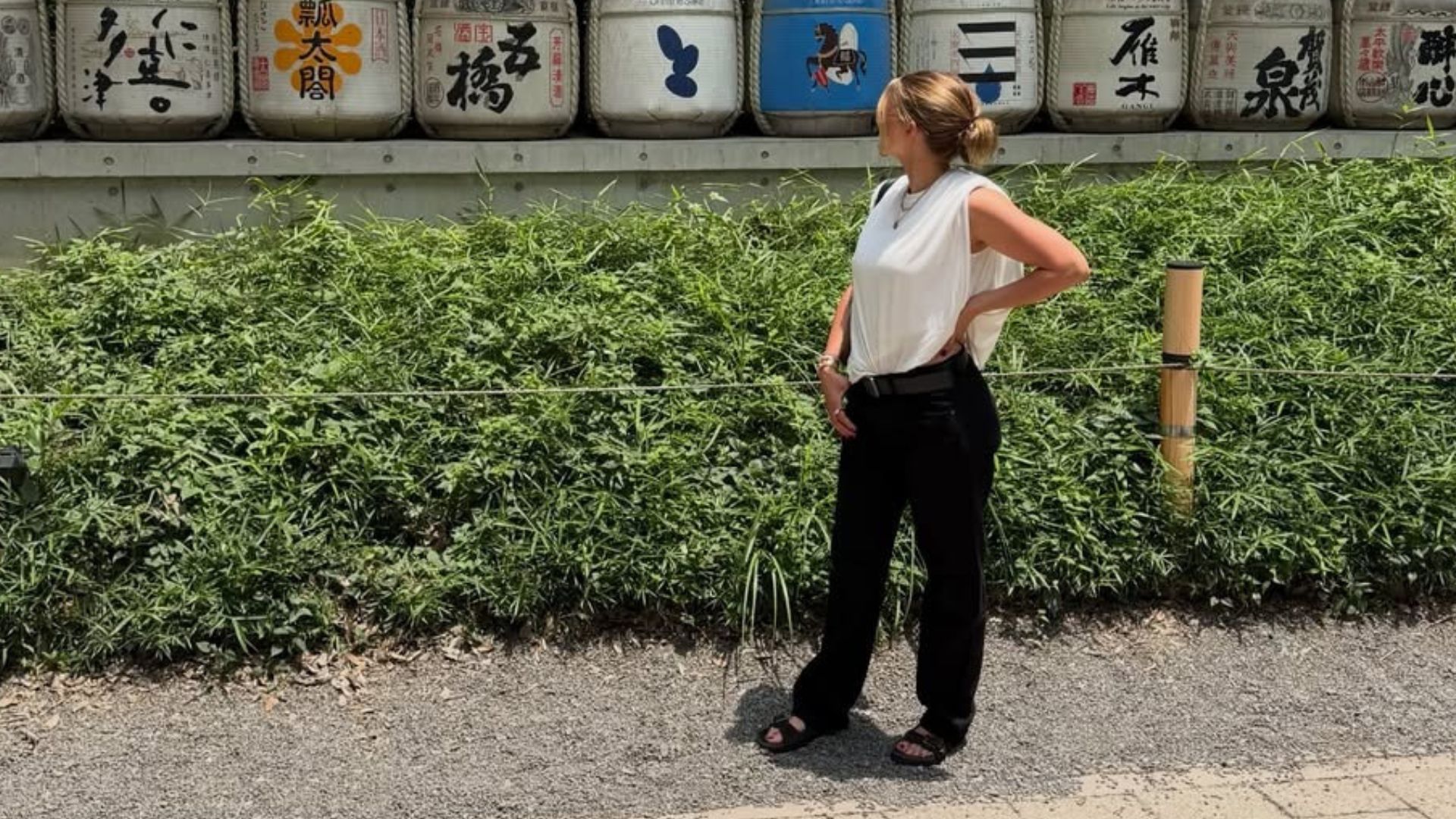 Sofia Richie Grainge poses for a photo wearing black trousers with black chunky sandals and a white top.