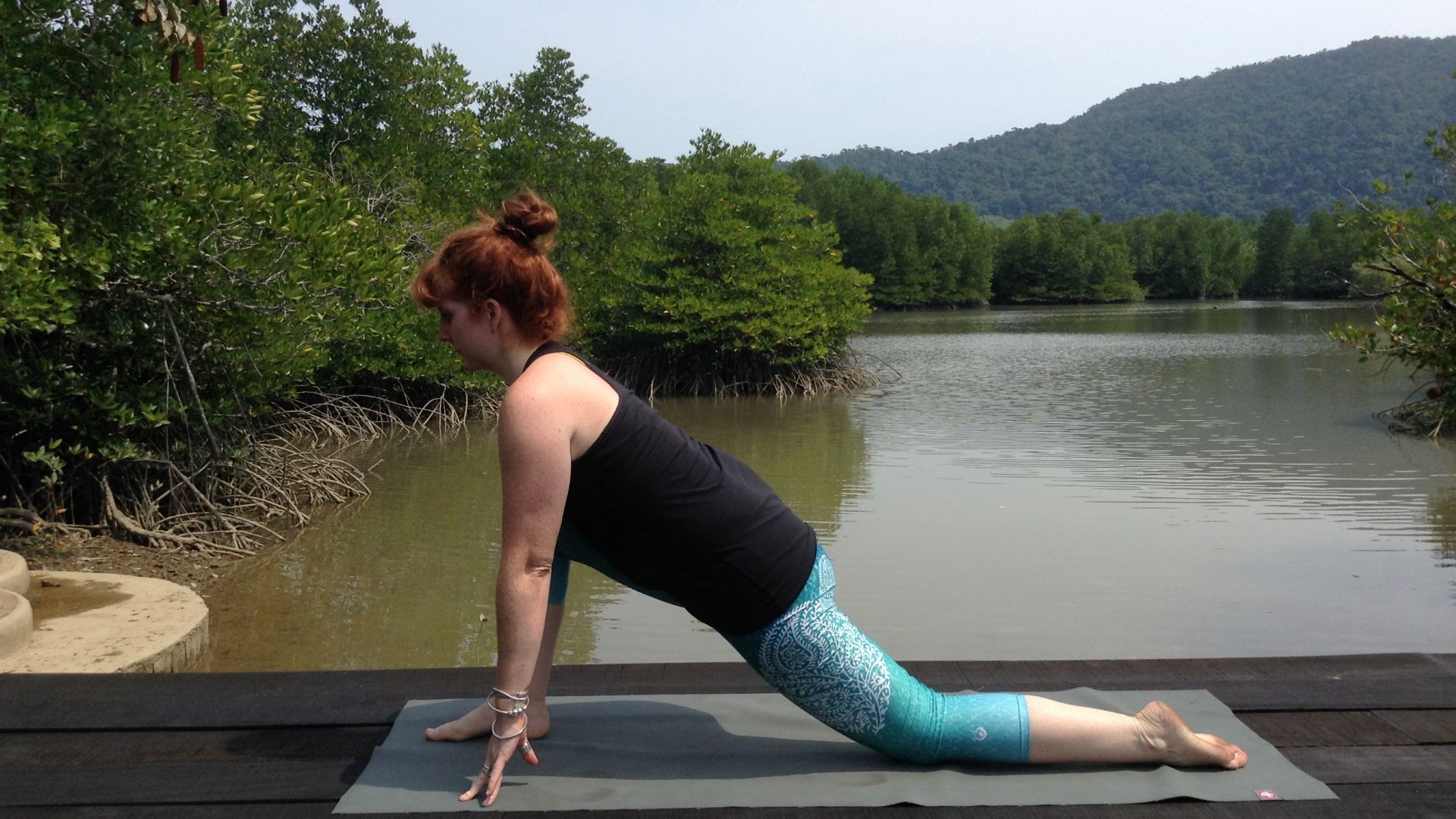 Yoga teacher Alison Reaume in low lunge pose. She is on a wooden platform with a lake and trees in the background