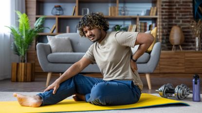 man sits on yoga mat holding his back in pain