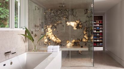 enclosed shower with backlit onyx wall with shower bench seat. elsewhere in the open bathroom is a built-in bath, and a doorway into the bedroom