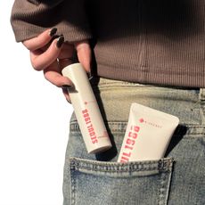 a woman wearing jeans pulling out a white and pink bottle from her back pocket