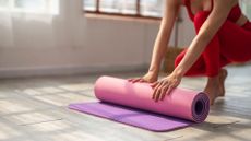 partly visible woman rolls up yoga mat on floor