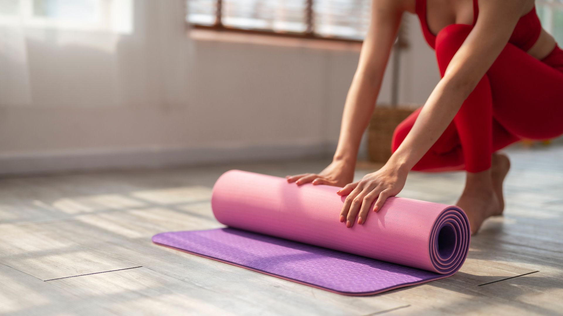 partly visible woman rolls up yoga mat on floor