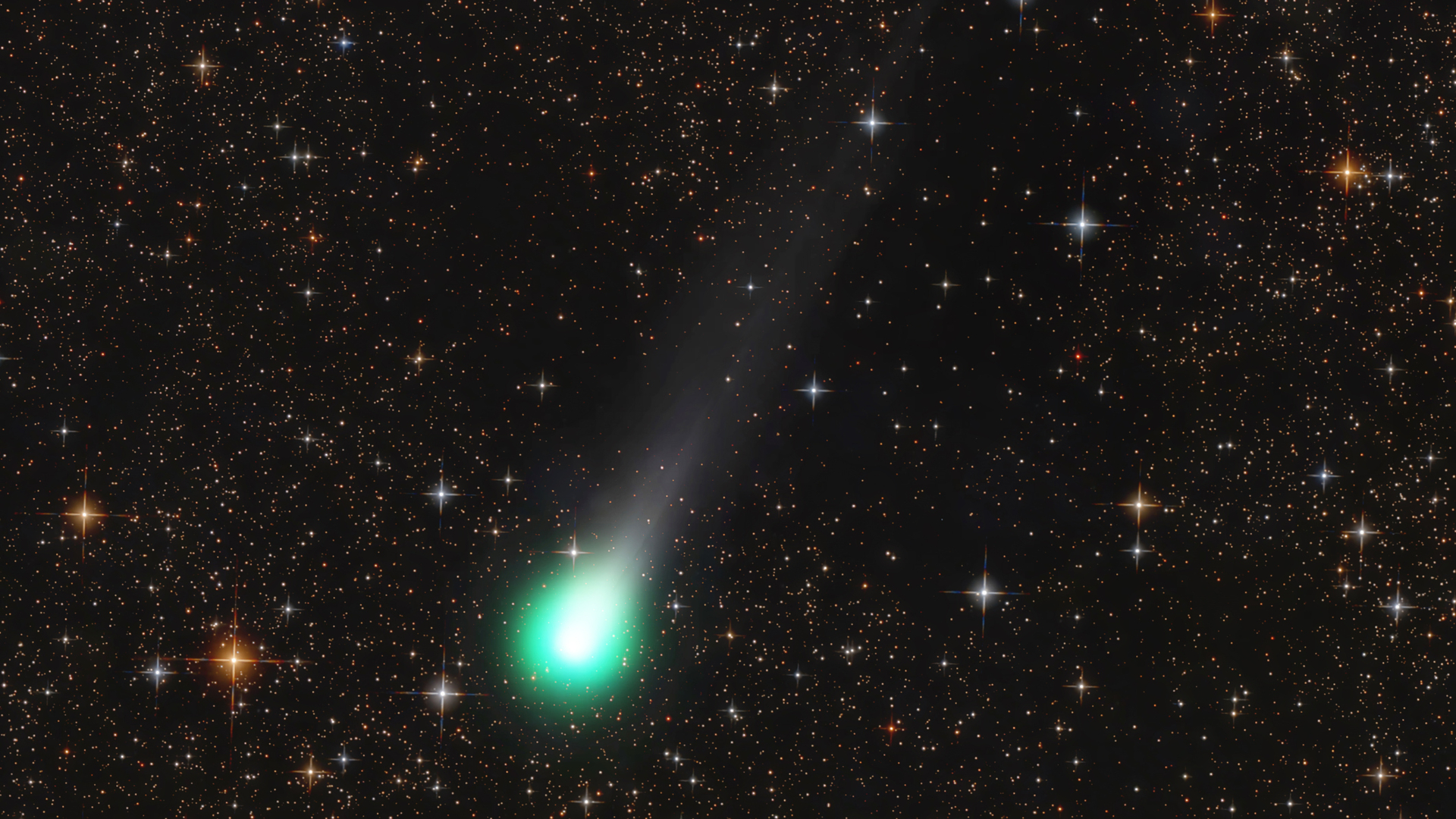 A green ball of light showing comet Lemmon streaks across an orange and black night sky full of stars.