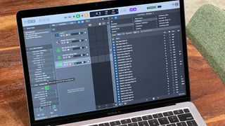 Photograph of Logic Pro open on a MacBook Air that's sitting on a wooden table. A green chair is visible off to the right.