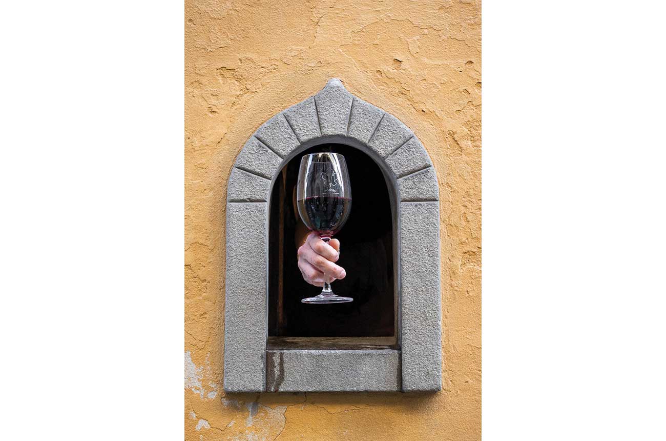 A wine window built into a palazzo in Florence with a hand holding a glass of red wine being offered