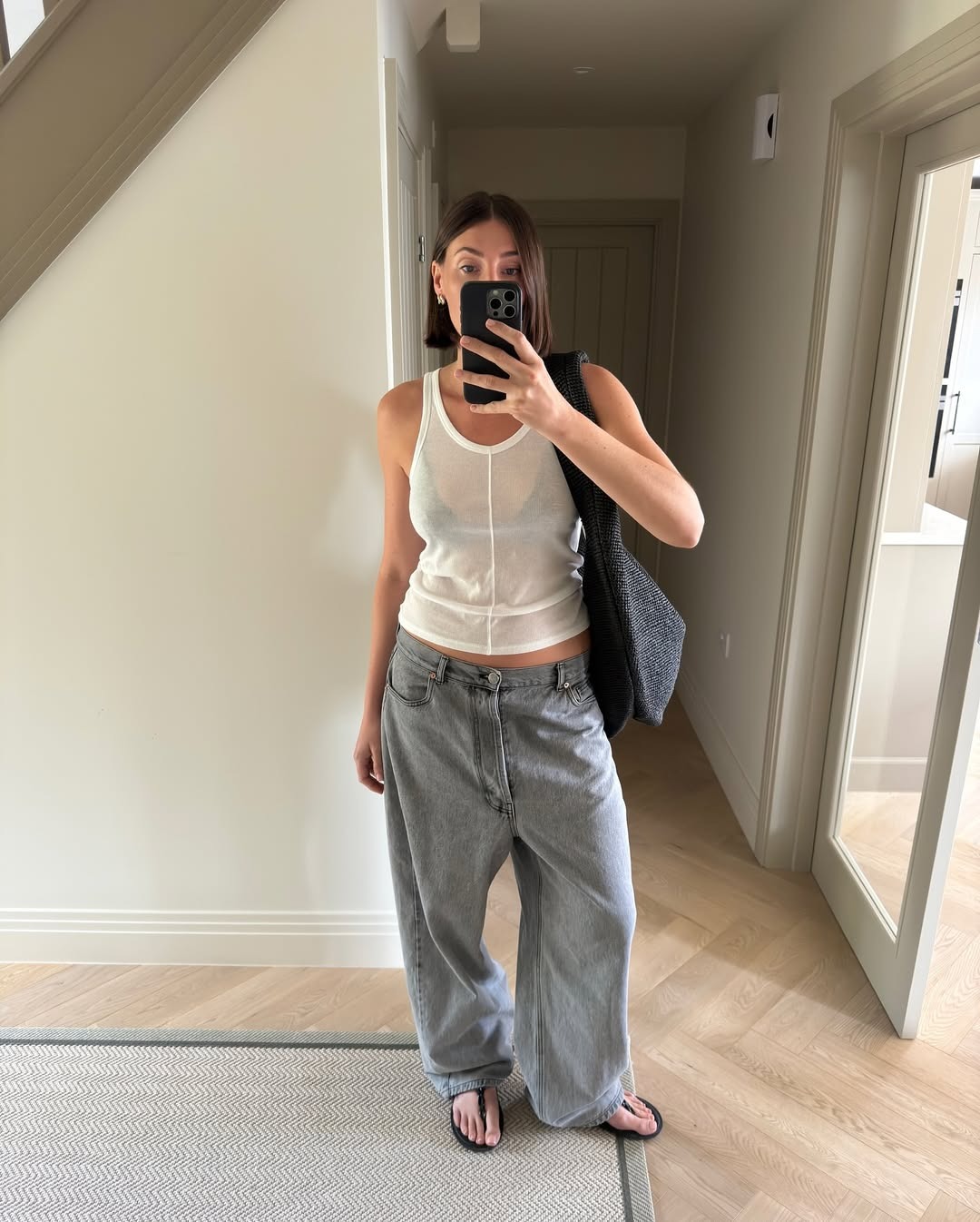 Influencer Sarah Louise-Blythe wears a white scoop neck top with baggy jeans, sandals, and an oversized woven bag.