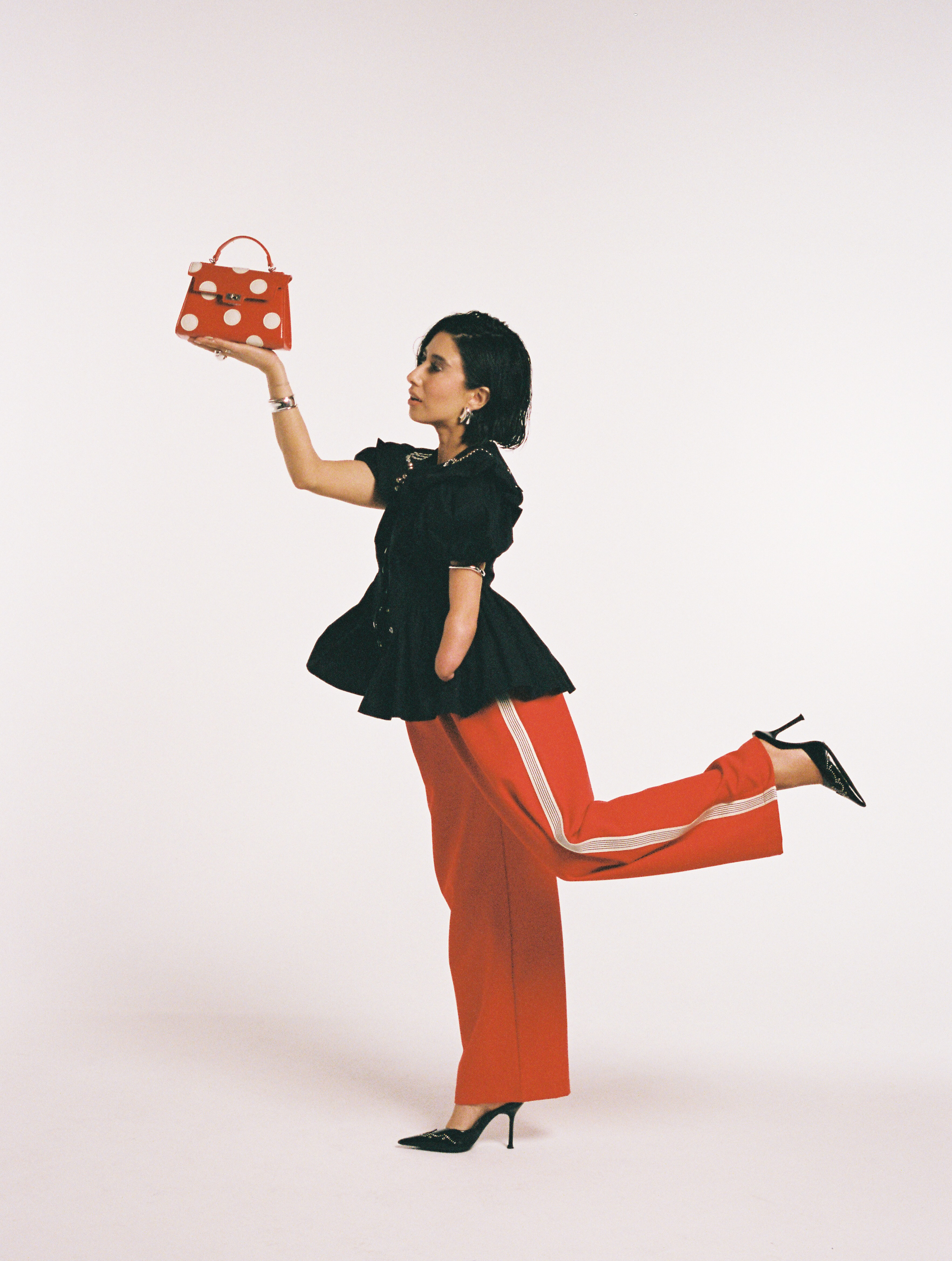 April Lockhart in red track pants, a black top, black heels, and red and white polka dot bag