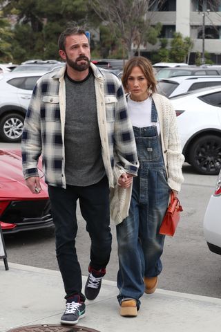 Jennifer Lopez and Ben Affleck walking hand in hand, Lopez wearing denim overalls with a cardigan and UGG platforms.