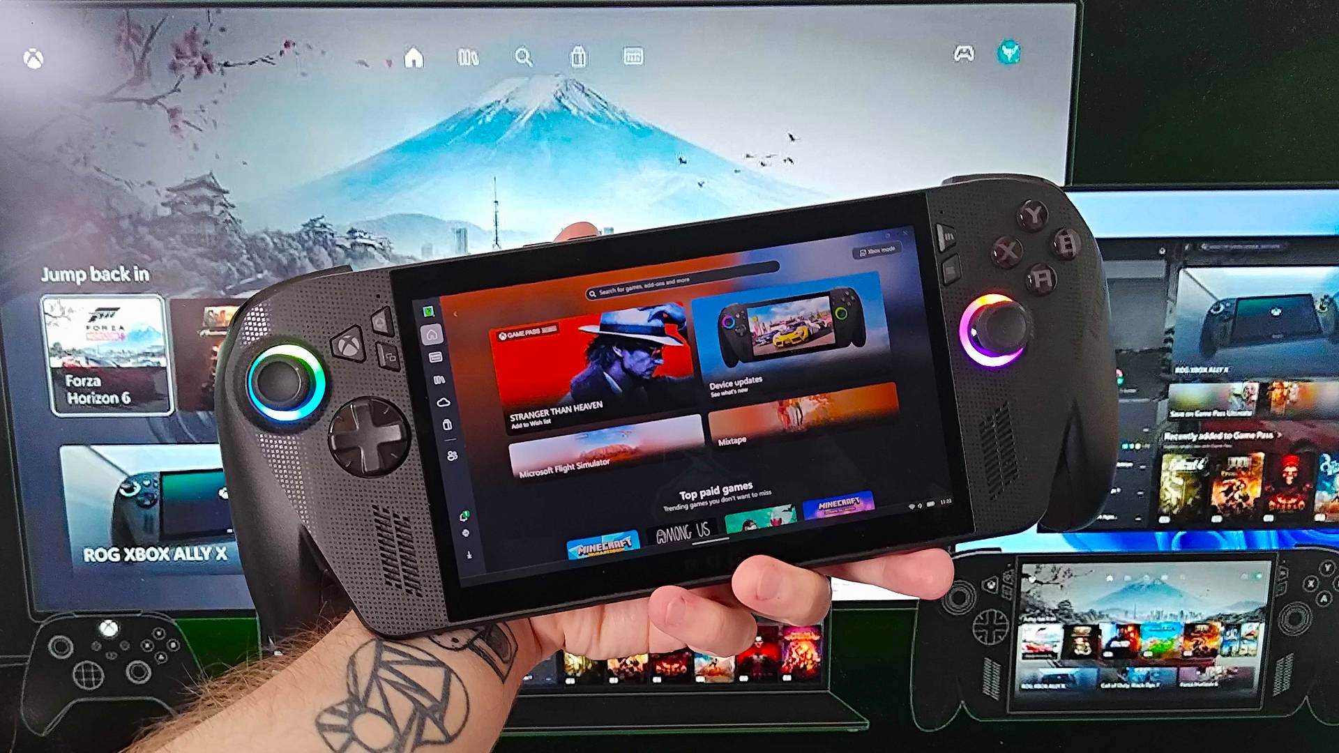 Hand holding ROG Xbox Ally X in front of monitor with Xbox "Consistent Experience" graphic displayed with devices using same UI.