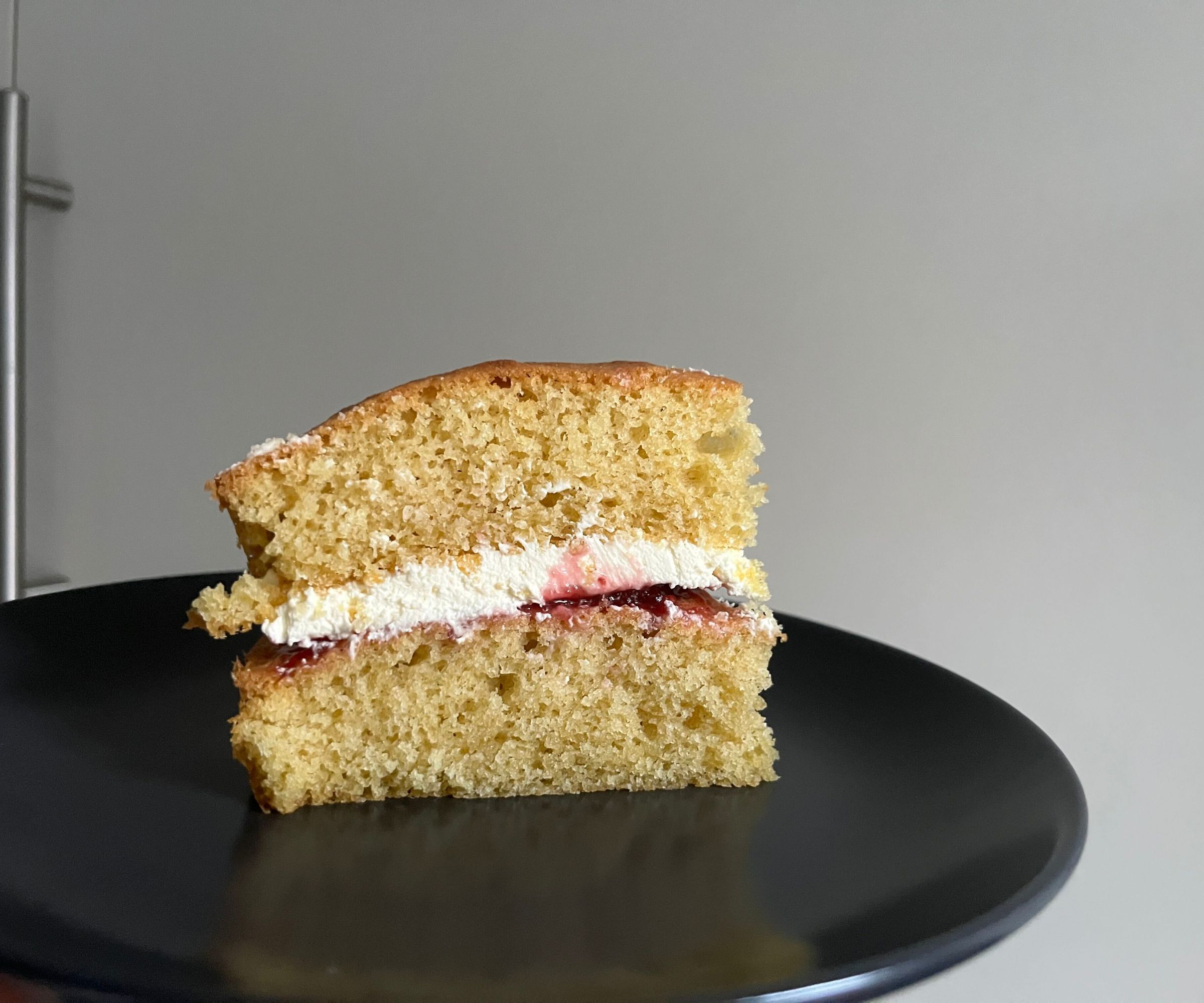 A slice of vanilla sponge cake with cream and jam layers inside