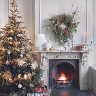 A white living room with a fireplace with a wreath above it and Chirstmas tree