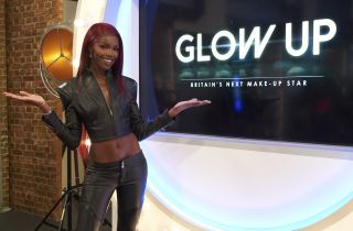 Model Leomie Anderson posing in front of the Glow Up sign in a leather jacket and trousers