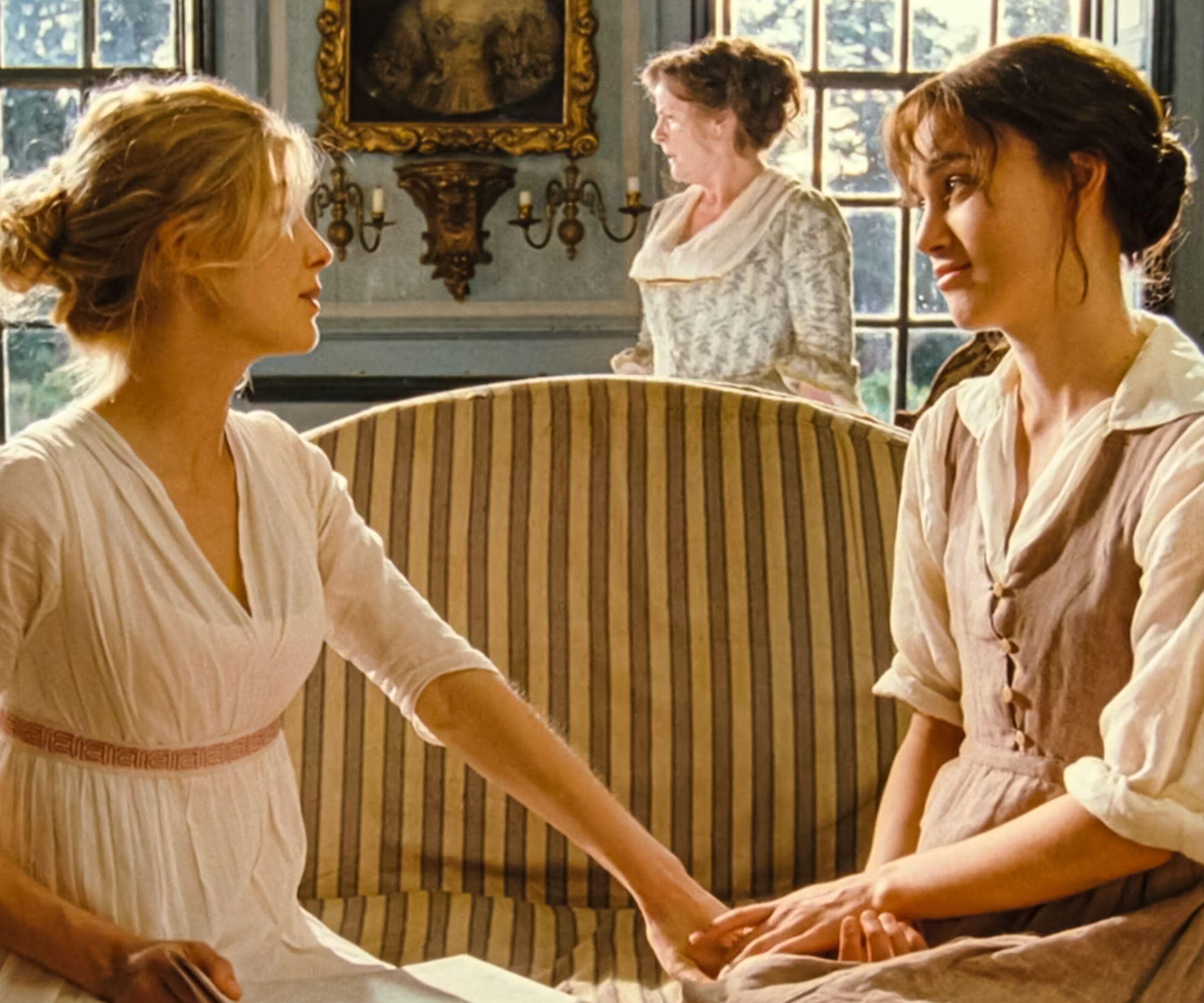 Keira Knightley and Rosamund Pyke in a traditional living room with striped sofa and large windows and painting