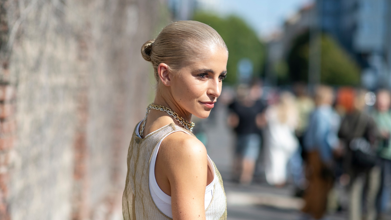 a woman with platinum blonde hair wearing a slick back bun with a white tank top in a side profile shot
