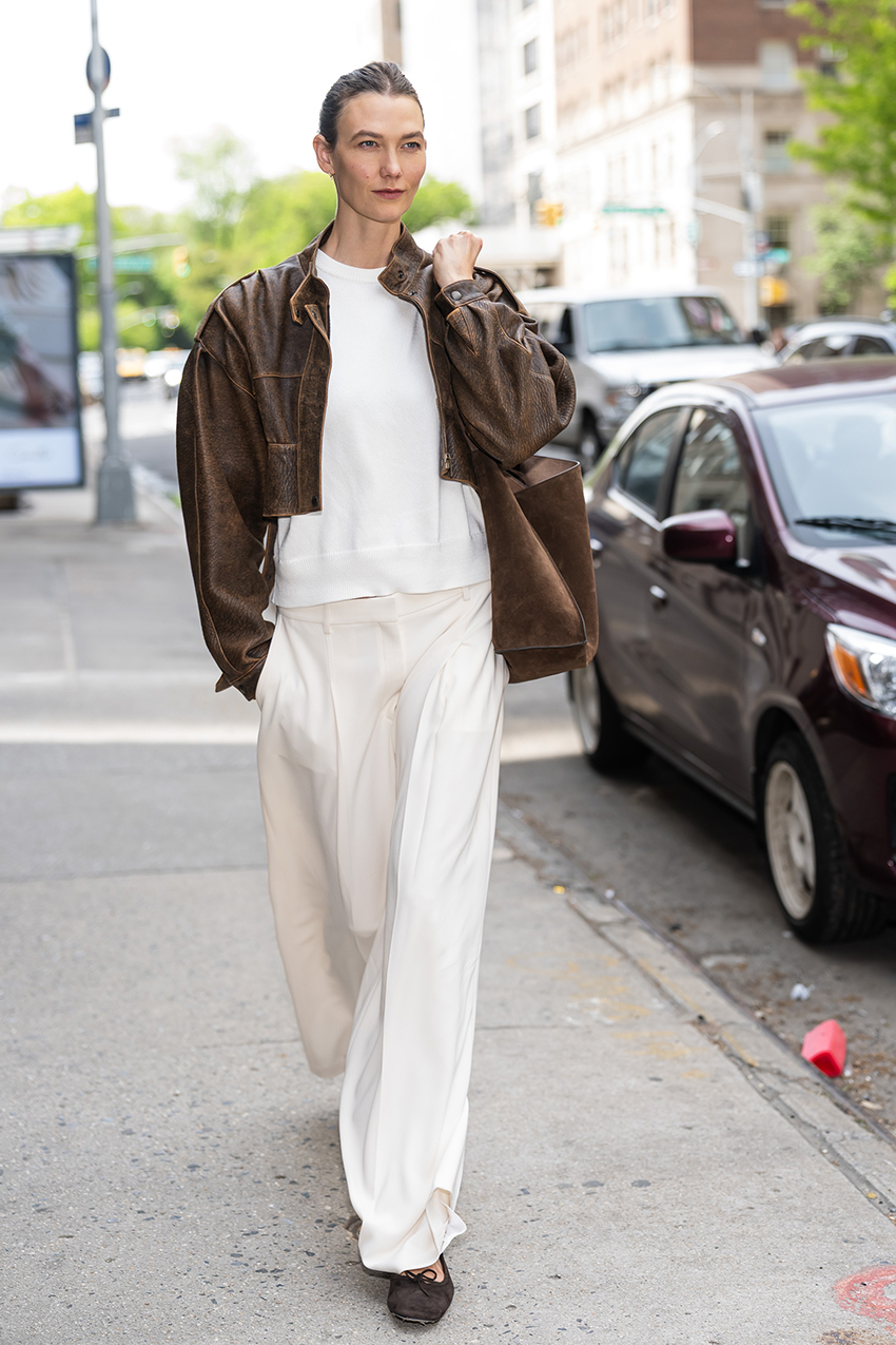 Karlie Kloss wearing a brown leather jacket, white tee, white pants, and black flats
