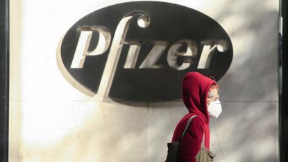 A woman wears a face mask as she walks by the Pfizer world headquarters in New York.