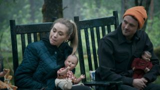 Gabby Windey and Dylan Efron turning to watch while holding creepy dolls in a chair in the woods on The Traitors US Season 3.