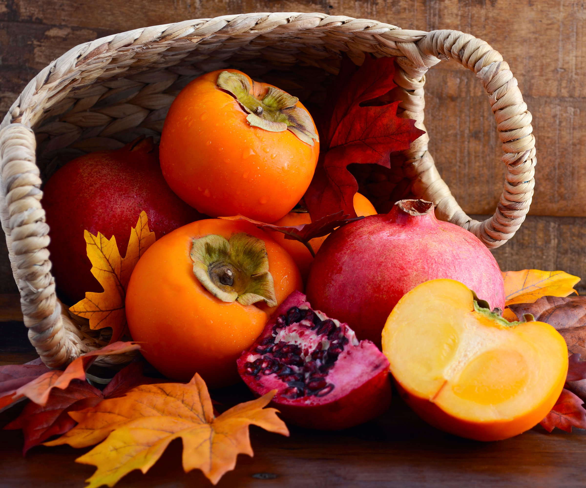 pomegranate and persimmon fruits in harvest basket with fall leaves
